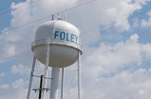 Photo of a Foley, MN white water tower against a blue sky with clouds, with the word "FOLEY" in all caps and light blue, posing the question, Are you looking for a bankruptcy attorney near me in Foley MN?