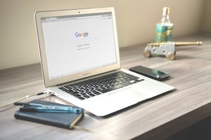 A laptop sits on a grey-wood desk surrounded by office supplies, open to Google to read law firm reviews about filing bankruptcy.