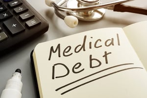 Closeup of a desk with a black calculator, stethoscope, black marker, and moleskin journal opened up to a page with MEDICAL DEBT written in marker and underlined twice, raising the question, Can bankruptcy help me with my medical debt in Minnesota?