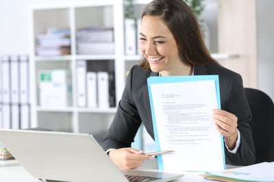 A smiling female Minnesota bankruptcy lawyer holds a up a piece of paper in front of a laptop with her chapter 7 bankruptcy client.