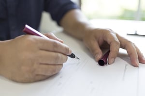 A man's right hand holding a pen and the left holding a pen cap over white paper forms and about to sign, posing the statement, Divorce decrees and bankruptcy in Minnesota: think before you sign.