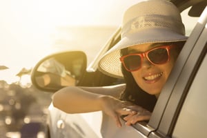 A smiling woman wearing a hat and red sunglasses leaning out of a car's driver's seat window asks the question, Will I lose my car if I file bankruptcy in Eagan, MN?