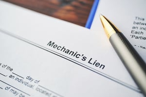 Pen and papers, one of which is titled "Mechanic's Lien" sit atop a dark wood desk, posing the idea of mechanics' liens and bankruptcy.