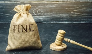 A light brown burlap sack with "FINE" in black letters across the front and a light wood gavel and block sit on a black marble tabletop against a distressed wood wall, posing the question, Minnesota bankruptcy fines and fees - what is dischargeable?