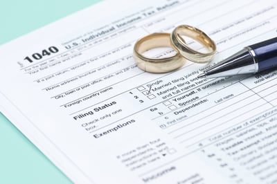 Two gold wedding bands and the silver tip of a pen lay on a 1040 tax form, laying on a mint-green colored surface, posing the statement, What to do when you owe joint tax debt in MN with a non-filing spouse or ex.
