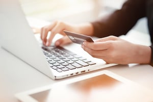 A woman's hands at a laptop, her left hand holding a debit car, posing the question, Should I continue to make payments while considering filing bankruptcy in Minnesota?