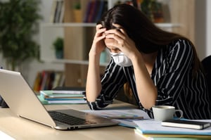 A woman wearing a COVID-19 mask, with her hands on her forehead in exasperation while sitting at a desk in front of her laptop, posing the question, What are my options for bankruptcy appointments in Minnesota during COVID-19?