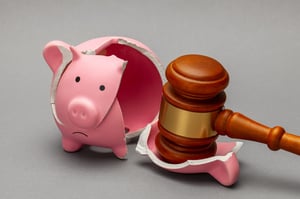 A previously smashed and now partially rebuilt pink piggy piggy bank next to a wood and gold gavel, posing the question, What happens during a bankruptcy case in Minnesota?