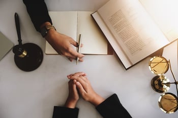 Overhead view of a desk with a law book, gavel and block, scales of justice statue, notebook, and the hands of a lawyer and client discussing a Chapter 13 plan modification in Minnesota.