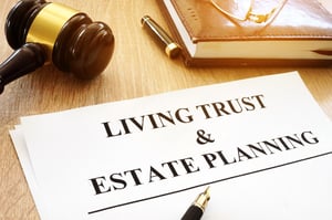 A bound book, pen cap, pen, gavel and paper on a light wood desk. The white paper has the words "LIVING TRUST & ESTATE PLANNING" written in black letters, posing the question, What Is a Trust in Minnesota?