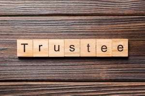 Wooden scrabble tiles spelling out "Trustee" on a thick-grained, dark wood table, posing the question, Who will be your bankruptcy trustee in Minnesota?