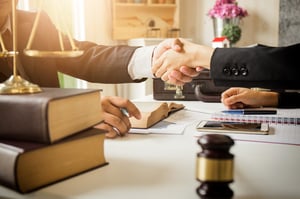 Closeup of a lawyer and client's shaking hands as they sit over a  legal desk with law books, a gavel, notebooks and other items, affirming why  one should seek counsel for a bankruptcy in Minnesota.
