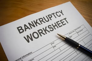 A wooden desk with a pen lying on a white sheet of paper titled "Bankruptcy Worksheet", giving information on filing bankruptcy.