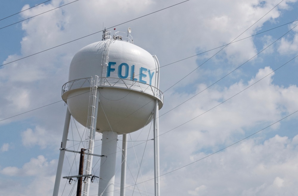 Photo of a Foley, MN white water tower against a blue sky with clouds, with the word 