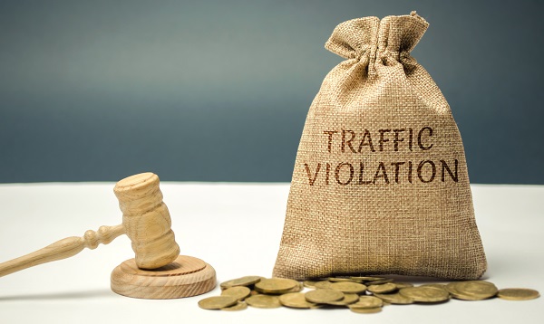 A white table and gray background with light wood gavel and block on the right, and a burlap sack of coins labeled TRAFFIC VIOLATION and around 20 loose coins on the left, posing the question, Can a bankruptcy in Minnesota wipe out my traffic tickets?