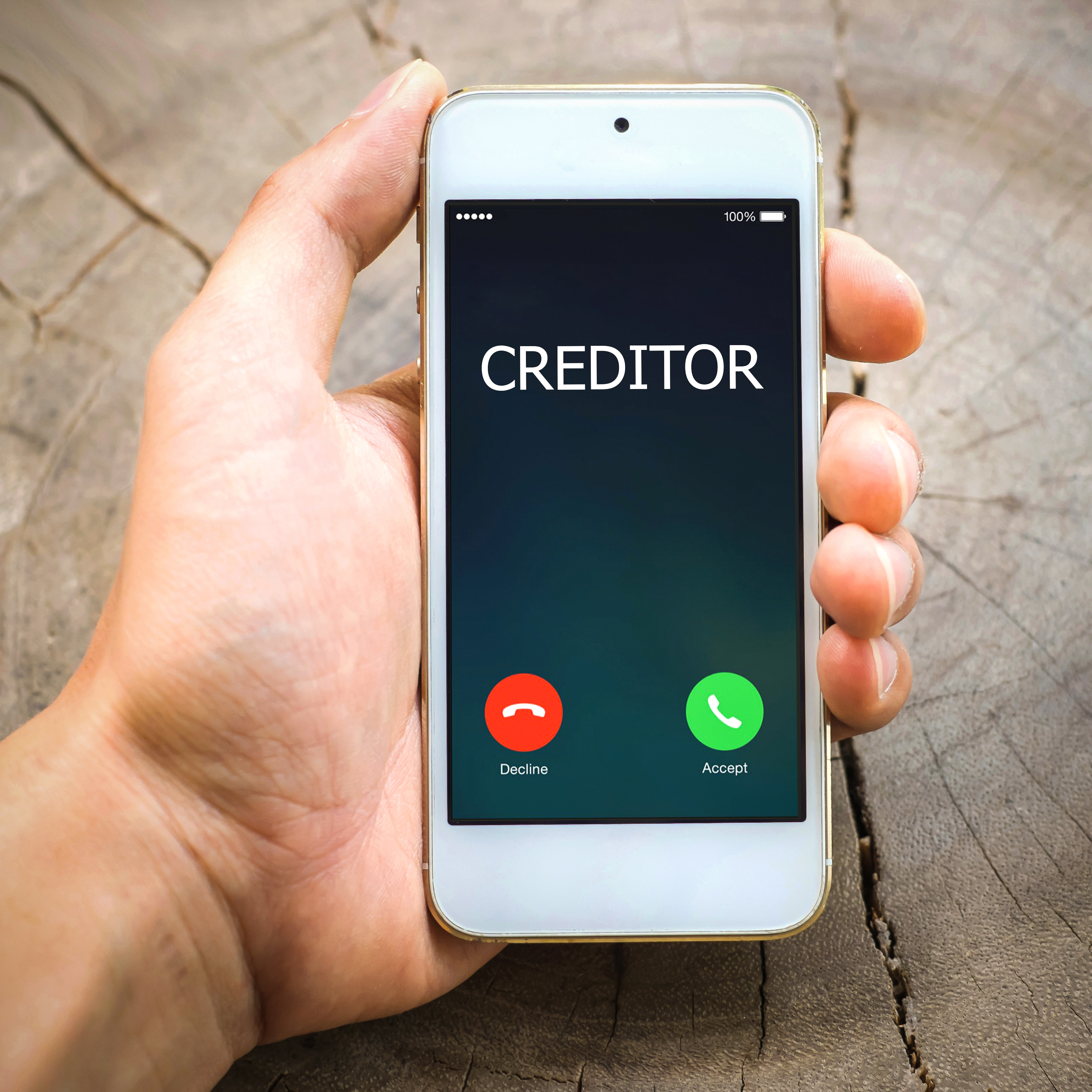 A hand holding an iPhone with the screen displaying an incoming call from a CREDITOR, representing how chapter 7 can protect you from creditors in Minnesota.