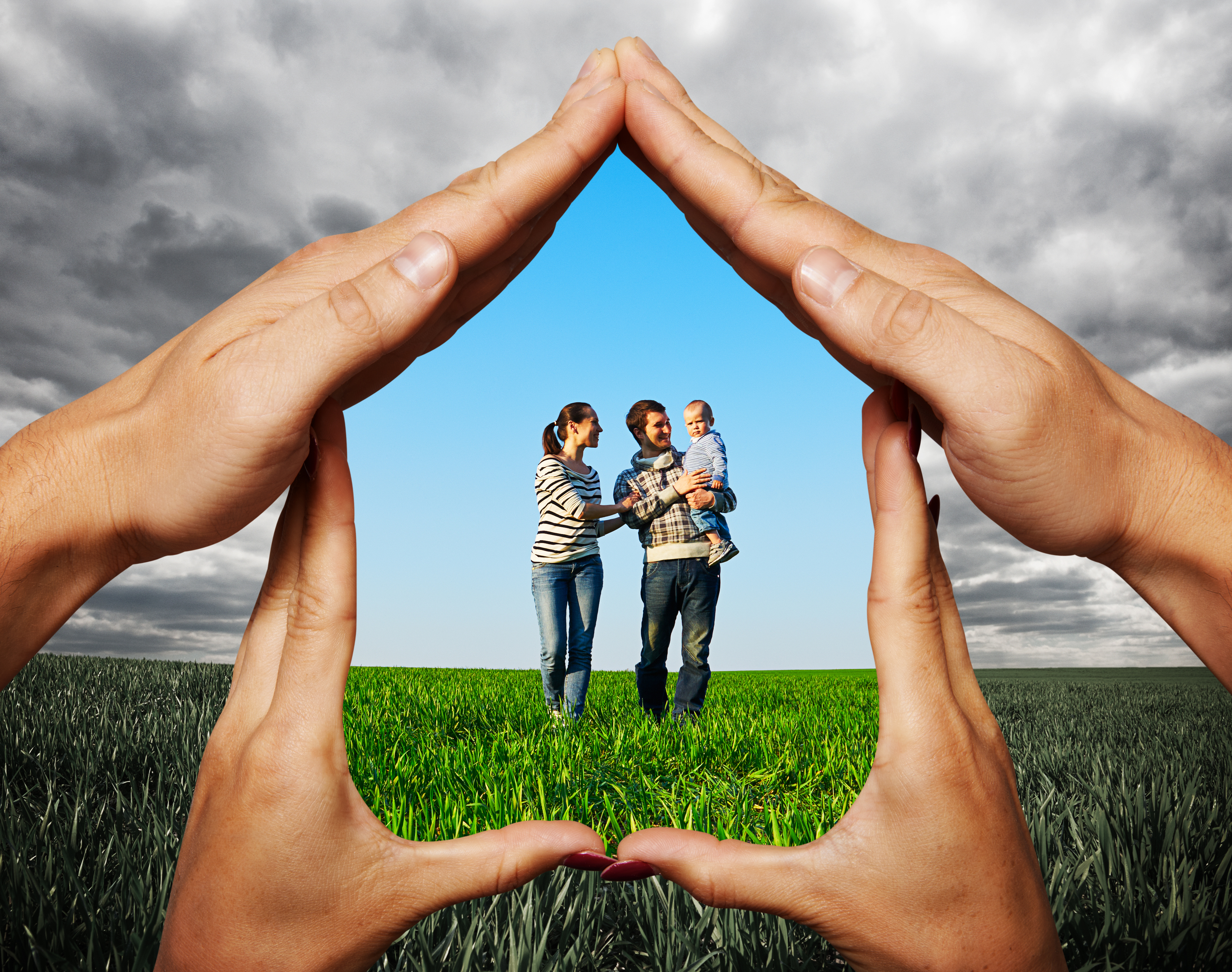 A family stands in the middle of a green field against the background of a bright blue sky. They are framed by four human hands, making the shape of a house. Inside the house the family is safe and in color, while outside, the color of the grass is darker and the sky is full of grey foreboding clouds, posing the question, How does filing bankruptcy protect me in Minnesota?