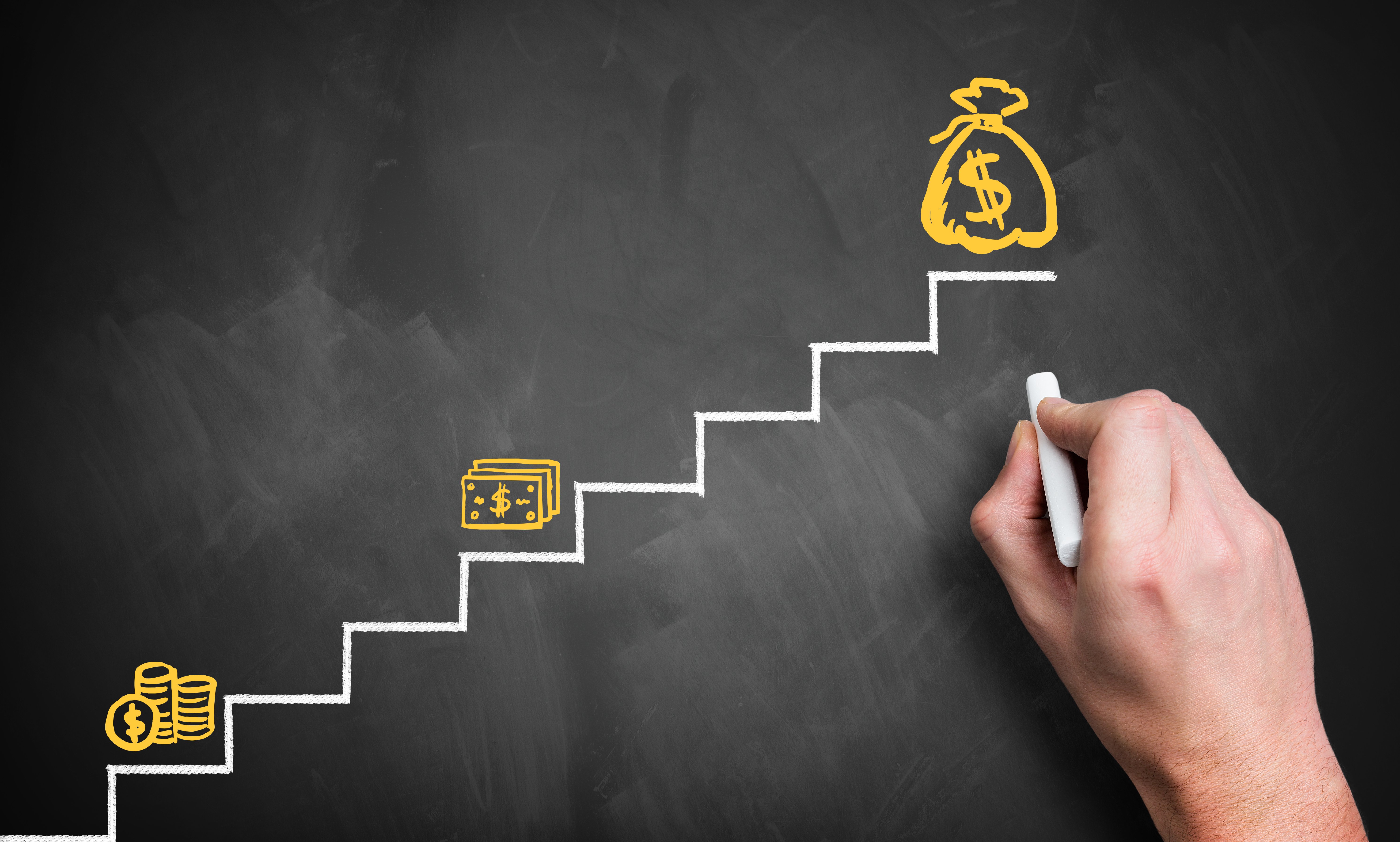 A hand draws on the far right side of a chalkboard, creating a simple staircase from left to right in white, and three images in yellow of a stack of coins, stack of paper currency, and a bag of money with a $ sign. The coins are on the first step, the paper currency on the fourth, and money bag on the eighth. The scene represents the question, If my income increases after the pandemic, will it affect my bankruptcy?