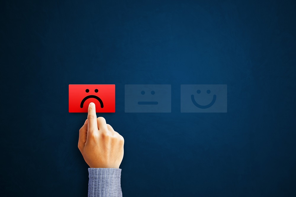 Closeup of a hand pushing a rectangular red button with a sad face on a blue background. Two other buttons, a light blue neutral face button and a light blue happy face button represent why Kain & Scott do not use any review software to game Google or BBB reviews.