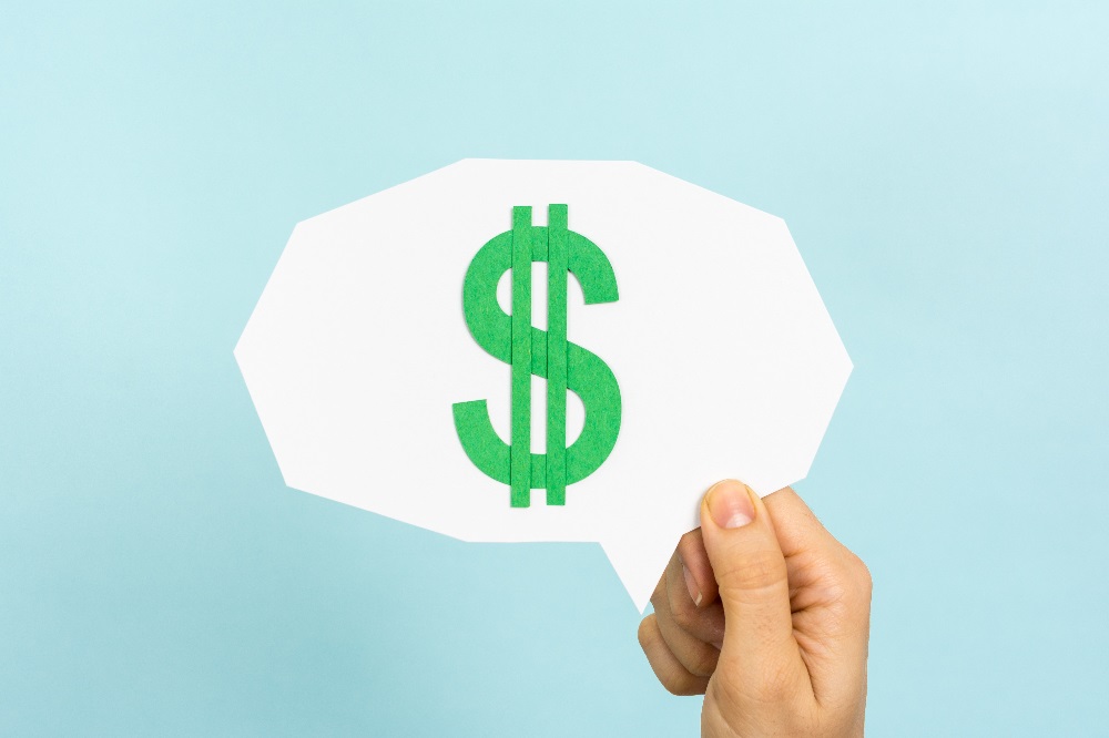 A hand holding a white conversation blurb with a green money sign in the middle, on a light blue background, posing the question, What Are Bankruptcy Preference Payments?