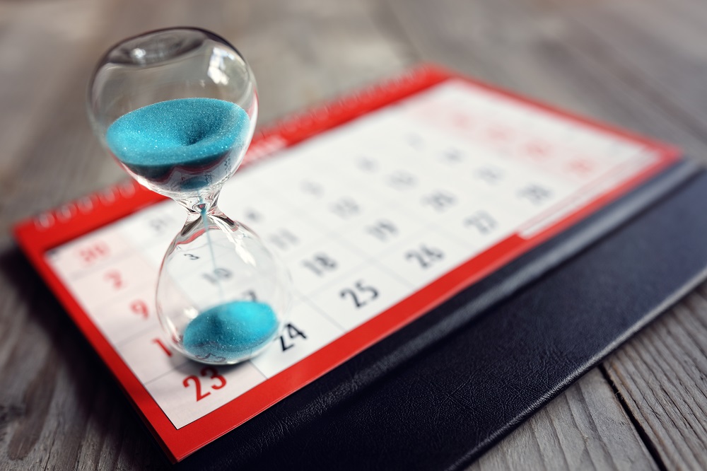A small hourglass filled with bright blue falling sand is set atop a personal calendar and cover, posing the question, What are the timing requirements for filing bankruptcy after a prior filing in Minnesota?