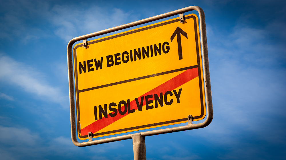 A  large, square, mustard yellow colored sign set against a background of blue sky that reads NEW BEGINNING with an arrow pointing upward across the top, and INSOLVENCY crossed out in red on the bottom.