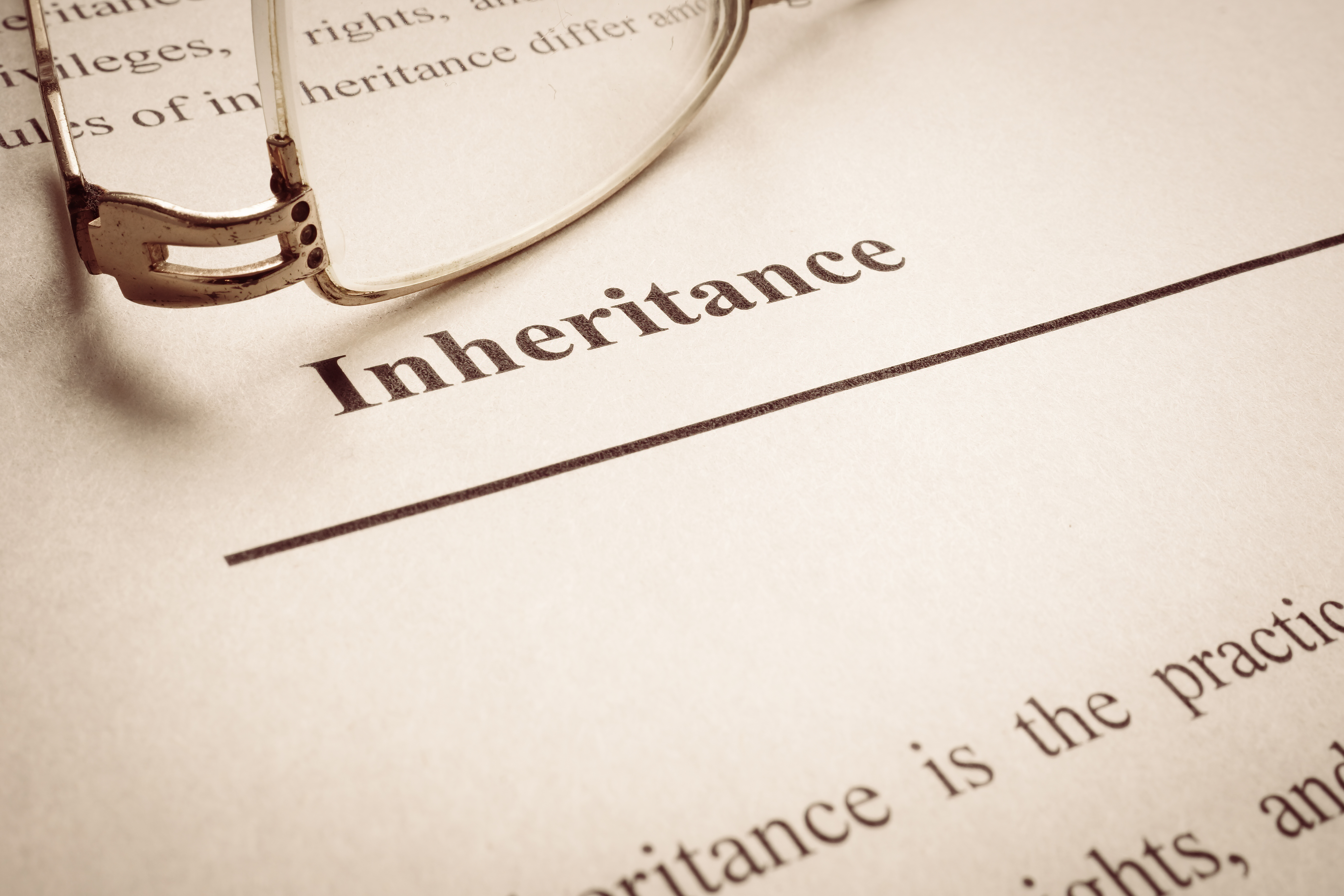 Closeup of a reading glasses lying on top of a piece of paper titled INHERITANCE with some visible text, posing the question, Why am I asked about receiving any inheritance during bankruptcy?