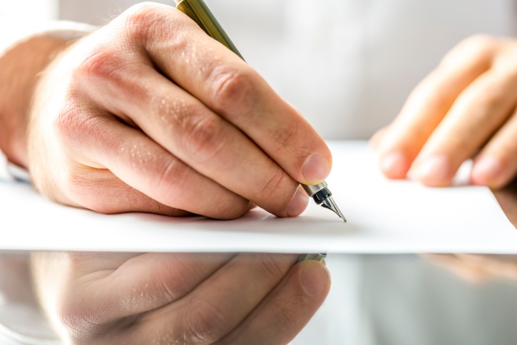 Hand holding a pen and writing on a white piece of paper containing the bankruptcy means test.