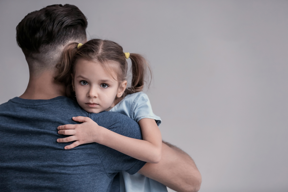 Sad little girl hugging her father on grey background