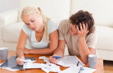 A male and female couple sitting at a desk full of bills wondering, Should I stop paying my bills before bankruptcy in Minnesota?